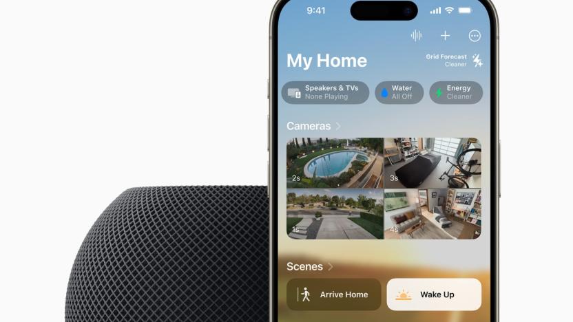 A HomePod mini in the color midnight (black) with an iPhone propped behind it. The image is cropped so only the top half of each device is show