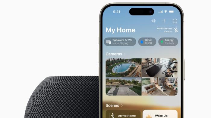 A HomePod mini in the color midnight (black) with an iPhone propped behind it. The image is cropped so only the top half of each device is show