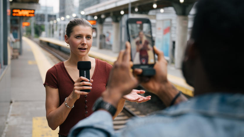 A person holding a mic, with another person filming them on a phone.