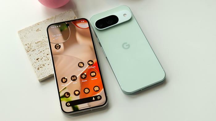 A Pixel 9 and 9 Pro laying on a table, one with its screen up and one with its rear camera facing up.