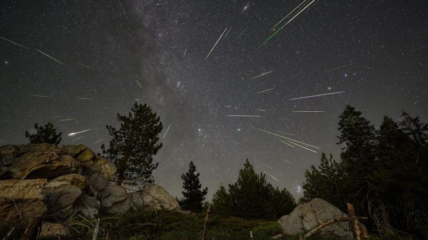 Streaks of light from the Perseid meteor shower are seen over a mountain landscape with boulders and trees