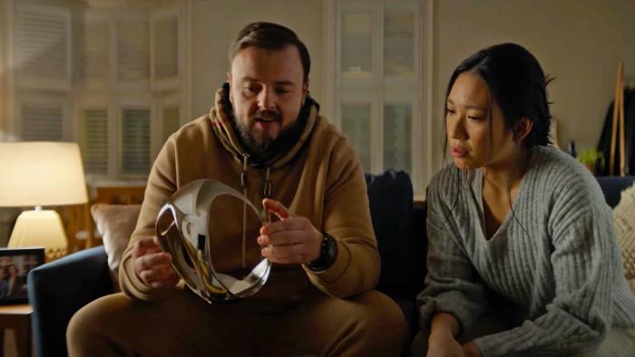 A man and woman sit on a living room couch and both look at a shiny object that the man is holding.