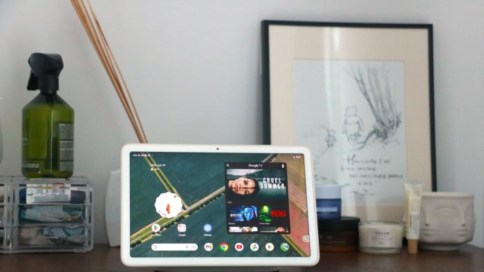 The Pixel Tablet on its dock on a walnut chest of drawers showing the Android home screen. 